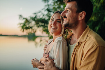 Happy couple embracing and admiring sunset over lake