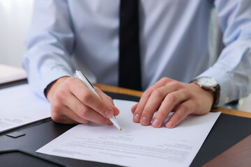 Notary signing document at table in office, closeup
