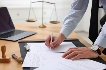 Notary signing document at wooden table in office, closeup