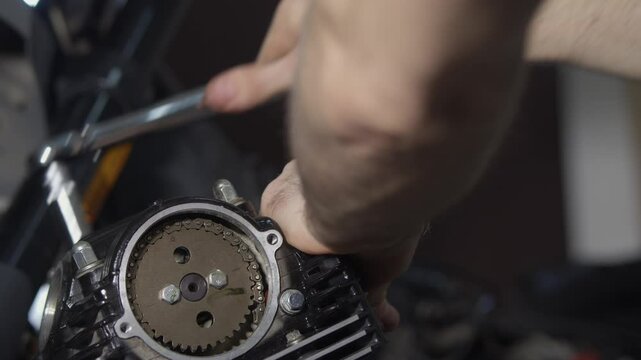 A mechanic is repairing a motorcycle engine, he is tightening the cylinder head nuts with a torque wrench