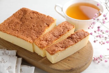 Cut tasty Japanese Castella sponge cake, tea and gypsophila flowers on white wooden table, closeup