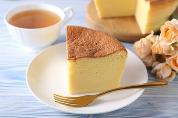 Tasty Japanese Castella sponge cake, tea, flowers and fork on light blue wooden table, closeup