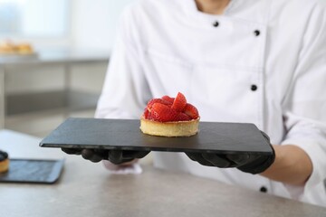 Confectioner with tasty tart at grey table in kitchen, closeup