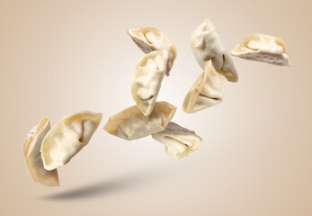 Uncooked gyoza falling on dark beige background