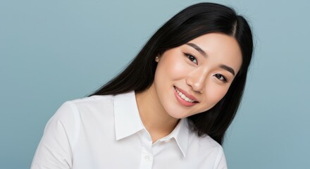 Obraz premium Asian woman with long black hair wearing white shirt isolated on blue background. Professional portrait for beauty, fashion, or corporate branding with minimal style.