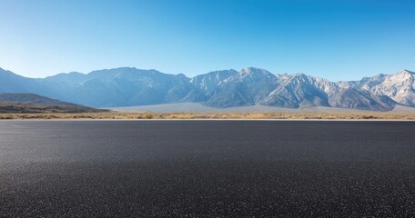 Empty asphalt road stretching into a mountain range under a clear sky