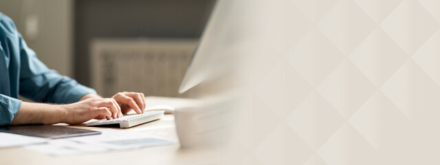 Young man sitting at desk and typing on computer keyboard, cropped shot of guy employee using pc in office, working online, businessman answering emails, side view, closeup