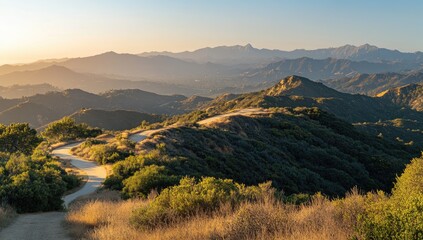 Scenic mountain vista at golden hour. Winding mountain road leads into a valley, surrounded by lush vegetation and distant hazy mountains. Sunlight bathes the landscape in warm tones