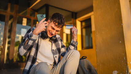 man student sit on stairs outdoor use mobile phone and credit card