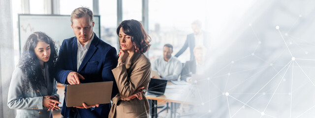 A group of business professionals are gathered around a table in a modern office setting. One man...