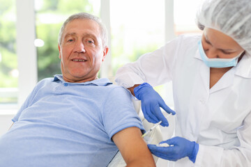 Fototapeta premium Adult woman doctor in medical uniform makes injection in arm of elderly man in medical office