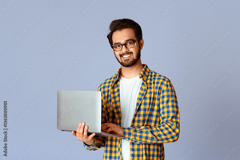 Poster happy indian guy with laptop computer working or studying online on lilac background