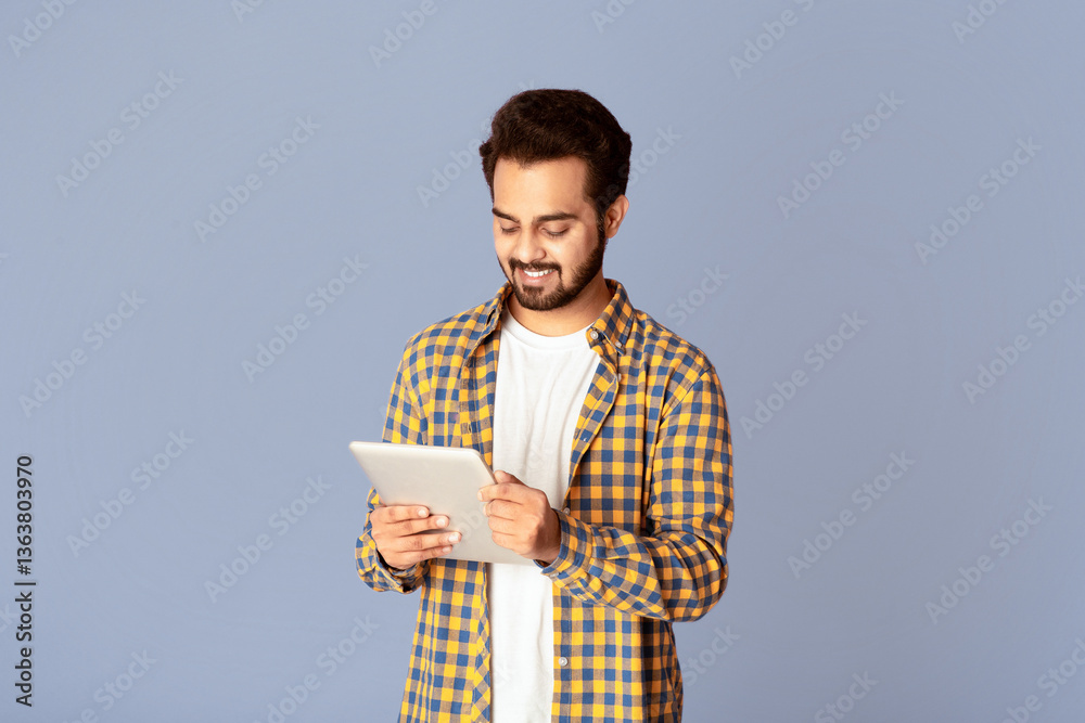 Poster smiling indian man studying or working online on tablet computer against lilac background