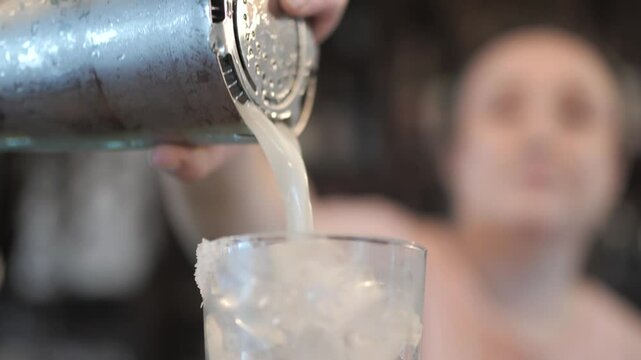 Female Bartender Pouring Margarita into Glass of Ice in Slow Motion at Bar