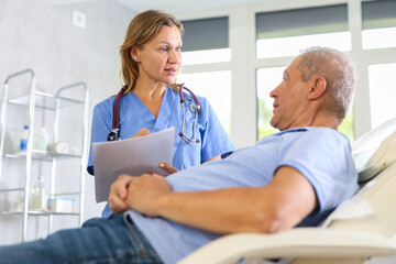 Obraz premium Female doctor conducts survey of elderly male patient after procedure and records data in client medical record