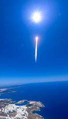 Rocket launch viewed from high altitude, bright sun, ocean and land visible below