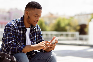 Obraz premium Technology Concept. Portrait of confident black hipster using cell phone, sitting outdoors, blurred background