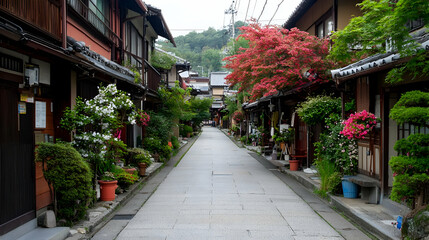 Fototapeta premium Picturesque Stone Paved Street Lined With Traditional Wooden Buildings and Lush Greenery with Pink Flowering Trees Under Daylight