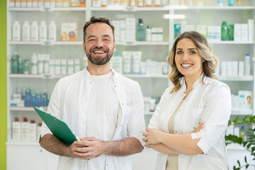 Obraz premium Two happy pharmacists pose and smile together in front of stocked shelves, emphasizing teamwork in healthcare.