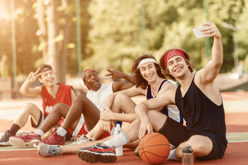 Team of basketball players taking selfie together after training at outdoor arena, copy space © Prostock-studio