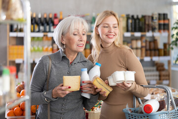 Two women shopper with various dairy products in her hands continues to make choice in grocery...