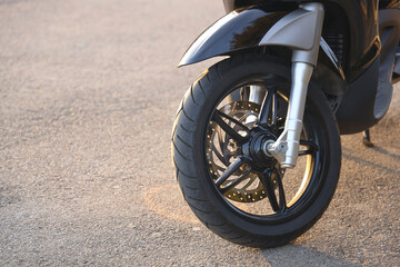 Close-up of wheel of modern scooter motorcycle parked on a beautiful asphalt road in perspective....