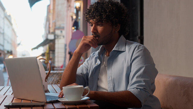Indian Arabian latino man visitor customer tourist in city cafe drink coffee thoughtful male freelancer business guy student businessman remote working laptop outdoor online studying internet shopping