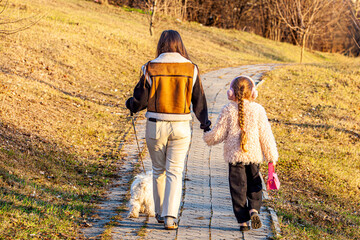 The picture on a beautiful sunny spring day shows two girls surprised as they strolled with a white-haired dog through the park that was just starting to green up, holding hands.