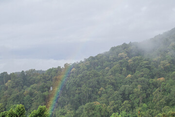 Fototapeta premium Beautiful rainbow in dramatic sky with fog morning creating a tranquil and magical scene. Nature landscape mountain.