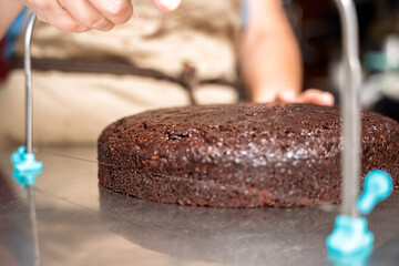 Pastry chef cutting chocolate cake with cake leveler wire in kitchen