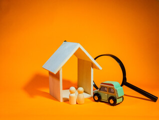 A wooden peg doll are standing near a wooden house, wooden car and a magnifying glass. The concept of property search, buying and selling. Apartments and car for rent. 