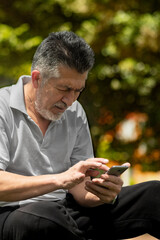 Older man texting and receiving messages on his cell phone in the park