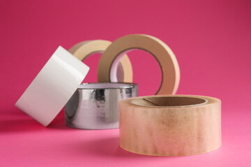 Rolls of different adhesive tapes on pink background, closeup