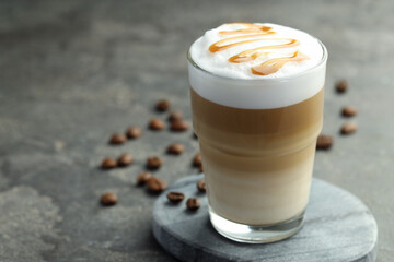 Tasty latte macchiato in glass and coffee beans on grey table, closeup. Space for text