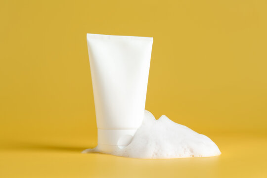 Tube of cosmetic product with foam on yellow background