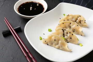 Delicious gyoza dumplings with chives and sesame seeds served on black table, closeup
