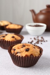 Delicious muffin with chocolate chips on light grey table, closeup