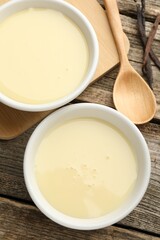 Tasty condensed milk, spoon and vanilla pods on wooden table, flat lay