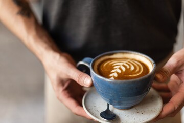 Man hands holding blue cup of coffee with latte art. Barista man holding blue coffee cup with latte art. Man holding coffee drink with latte art. Coffee and barista. Latte art in blue coffee cup
