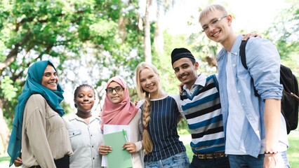 Fototapeta premium Diverse group of young adults smiling outdoors. Friends from various backgrounds, enjoying time together. Happy, diverse, and youthful group bonding. Diverse young friends in school park.