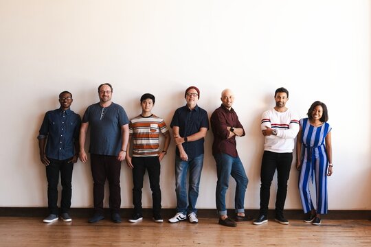 A diverse group of people standing in a line against a wall. Casual attire, mixed men and women. Group of friends or colleagues smiling together. Diverse startup business team starting in row.