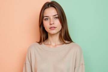 Fototapeta premium Portrait of a Young Caucasian Woman in a Casual Oversized Beige Sweater Against a Soft Coral and Mint Green Background