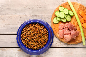 Bowl with dry pet food, raw meat and natural products on light wooden background