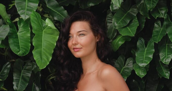 Gorgeous young woman with long dark hair posing confidently in front of vibrant tropical leaves. Perfect for concepts like natural beauty, tropical vibes, and outdoor lifestyle. 