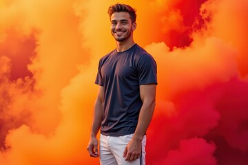 A Smiling Young Athletic Male in a Dark T-Shirt Posing Against a Dramatic Background of Orange and Red Smoke, Exuding Confidence and Adventure