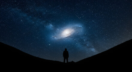 Fototapeta premium A silhouette of a person on a dark hillside under a brilliantly starry sky