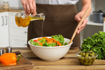 Woman adding olive oil into bowl with tasty salad at table in kitchen