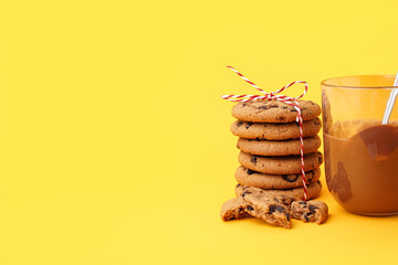 Tasty cookies with chocolate chips and glass of sauce on yellow background
