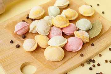 Wooden board of colorful raw dumplings with peppercorn and bay leaf on yellow background