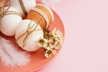 Plate with decorated Easter eggs, small flowers and feather on pink background